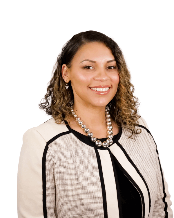 Woman with shoulder-length curly hair, wearing a cream and black jacket with a pearl necklace, smiling in front of a white background.