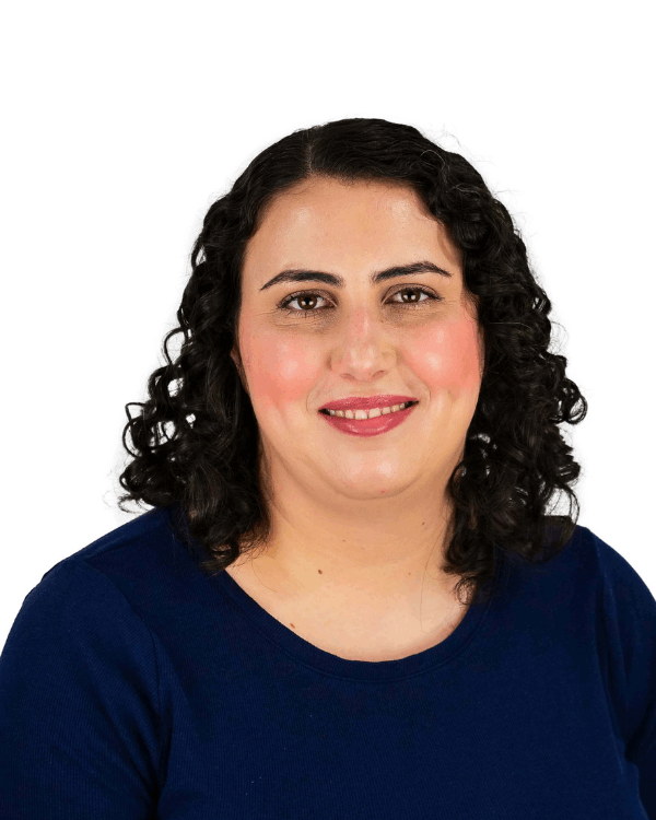Woman with shoulder-length dark curly hair, wearing a navy blue top, smiling gently in front of a white background.