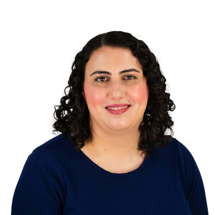 Woman with shoulder-length dark curly hair, wearing a navy blue top, smiling gently in front of a white background.