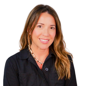 Woman with long wavy hair, wearing a black zip-up jacket and a chunky chain necklace, smiling against a white background.