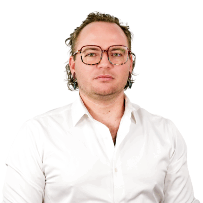 Man with wavy hair and tortoiseshell glasses, wearing a white button-down shirt, facing forward with a neutral expression.