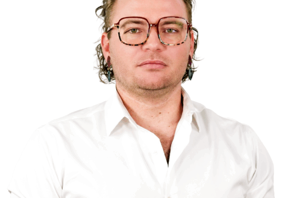Man with wavy hair and tortoiseshell glasses, wearing a white button-down shirt, facing forward with a neutral expression.