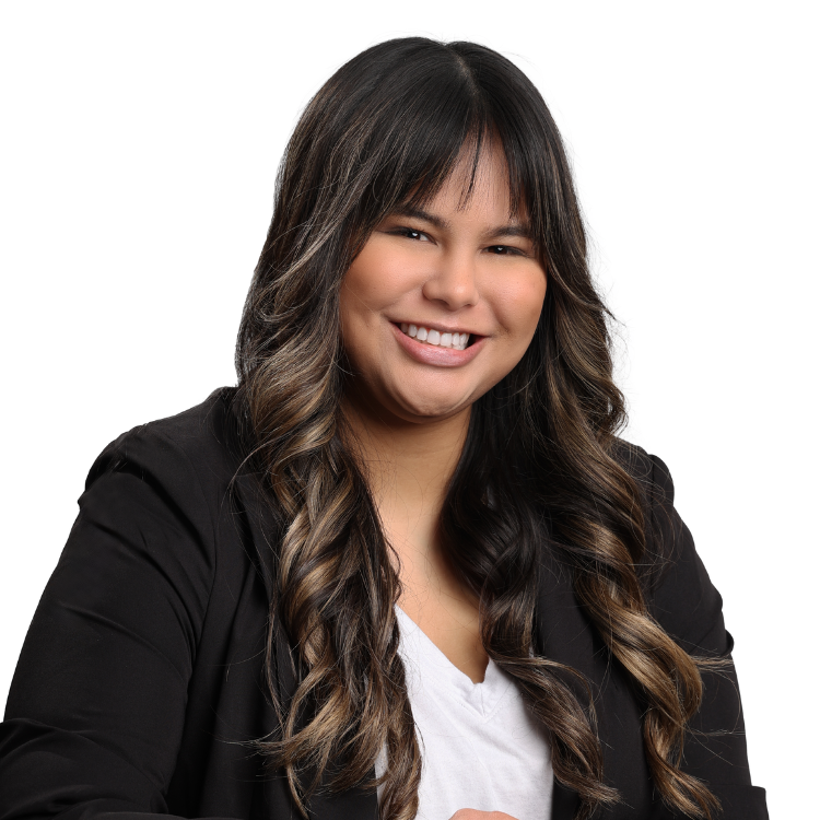 Woman with long, curled dark brown hair and bangs, wearing a black blazer and white blouse, smiling brightly in front of a white background.