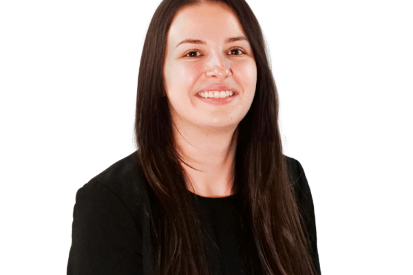 Woman with long straight brown hair, wearing a black top, smiling in front of a white background.