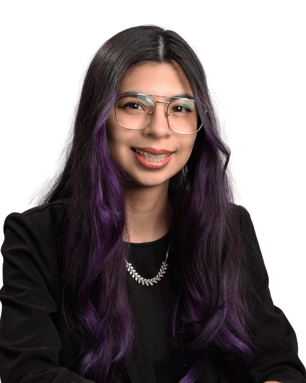 Woman with long dark hair dyed purple at the ends, wearing glasses, a black top, and a silver necklace, smiling gently in front of a white background.