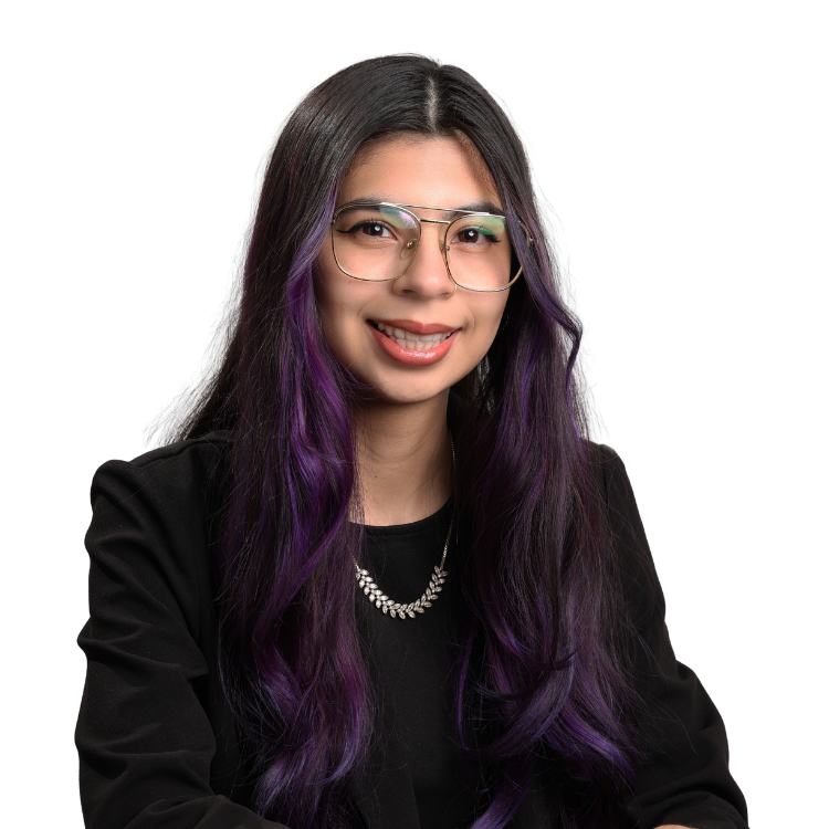 Woman with long dark hair dyed purple at the ends, wearing glasses, a black top, and a silver necklace, smiling gently in front of a white background.