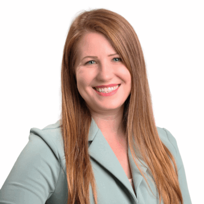 Woman with long straight red-blonde hair, wearing a light green blazer, smiling confidently in front of a white background.