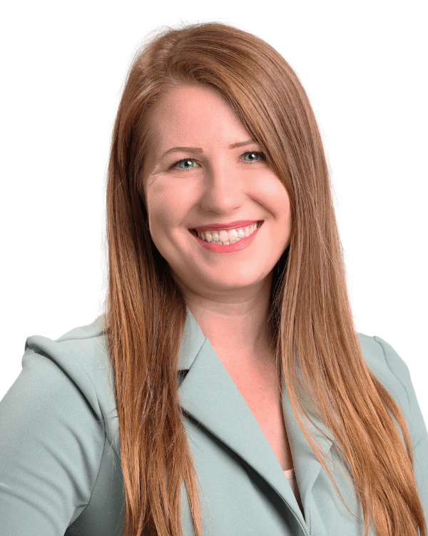 Woman with long straight red-blonde hair, wearing a light green blazer, smiling confidently in front of a white background.