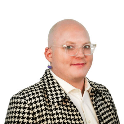 Bald person with clear glasses and a bold earring, wearing a black and white houndstooth jacket over a white shirt, smiling slightly.