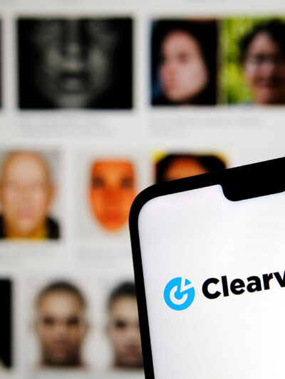 Clearview AI facial recognition software logo on the glowing screen and blurred faces from social media on the background