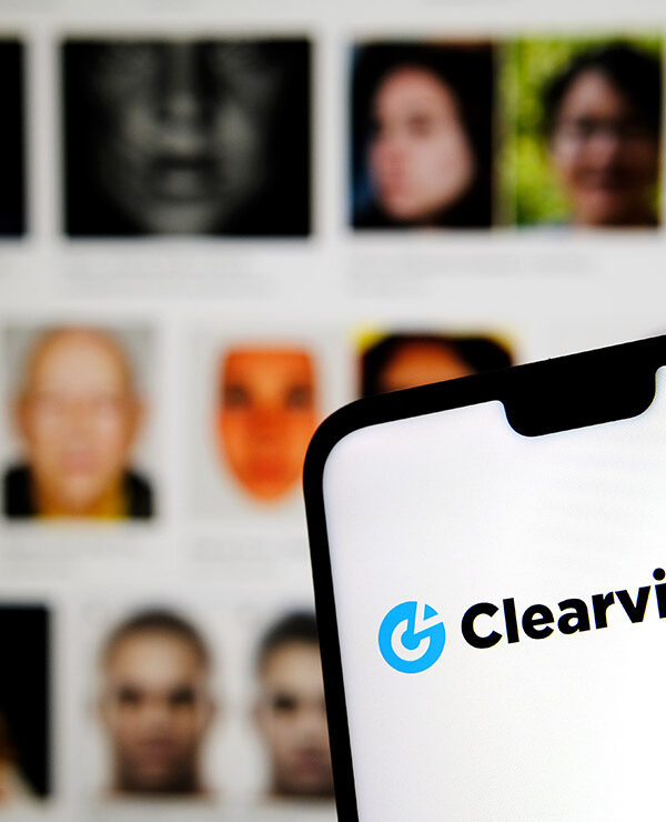 Clearview AI facial recognition software logo on the glowing screen and blurred faces from social media on the background