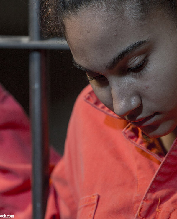 A incarcerated woman standing behind bars.