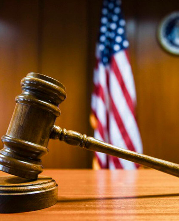 A gavel rests on the judge’s bench in a courtroom with American flag in the background.
