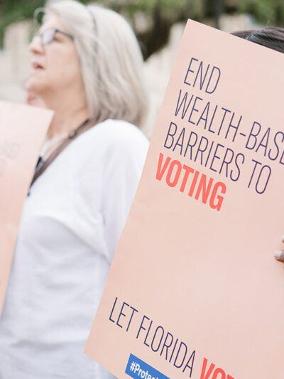 Woman holding sign reading 'End wealth based barriers to voting"