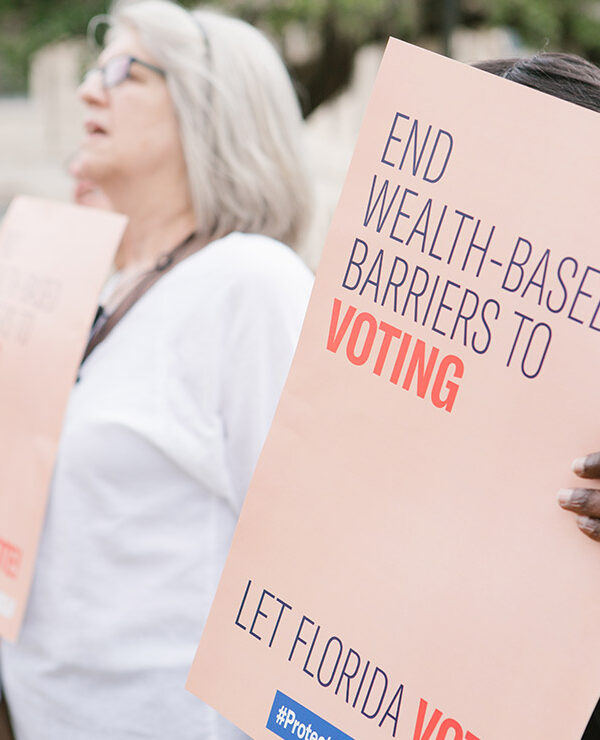 Woman holding sign reading 'End wealth based barriers to voting"