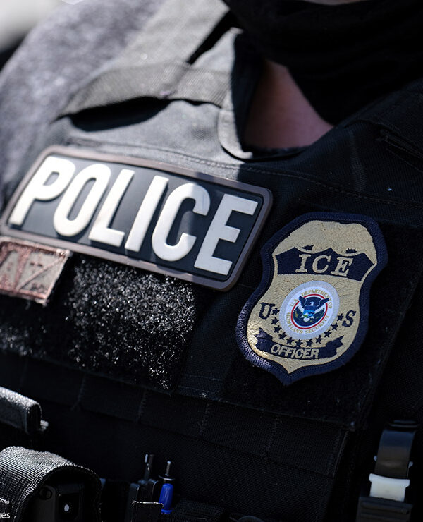 A close up of a police officer wears a "Police" label beside a U.S. ICE (standing for Immigration and Customs Enforcement) badge on his vest.