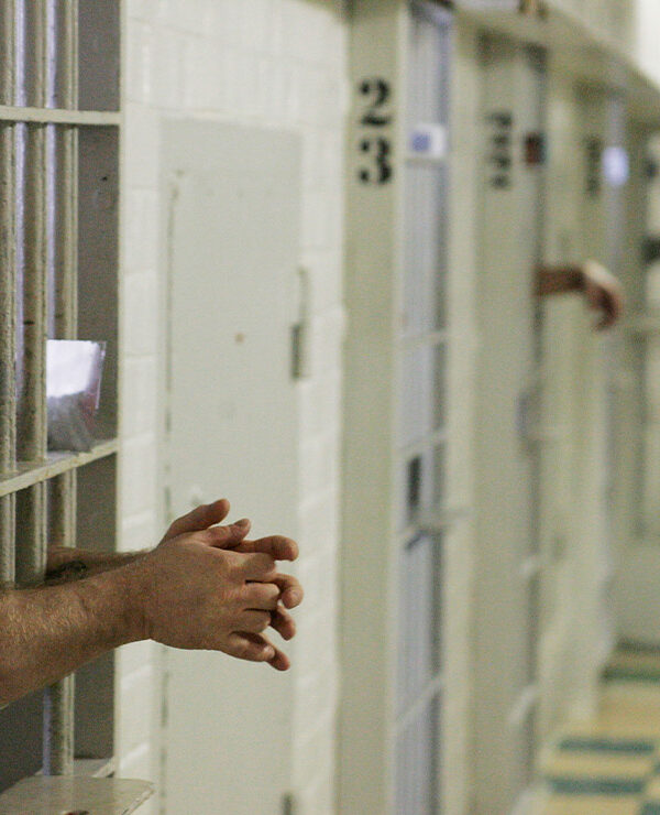 Prisoners reach through the metal bars of their cells.