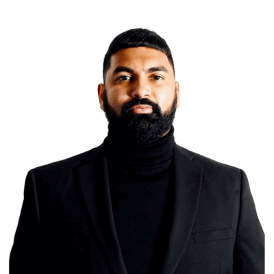 A man with a neatly trimmed beard and short hair, wearing a black turtleneck and a black blazer, stands against a plain white background.