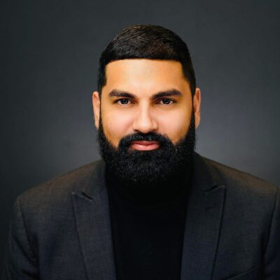 Athar Haseebullah. He is a Pakistani man with a full beard. He is wearing a black turtle neck and grey blazer.