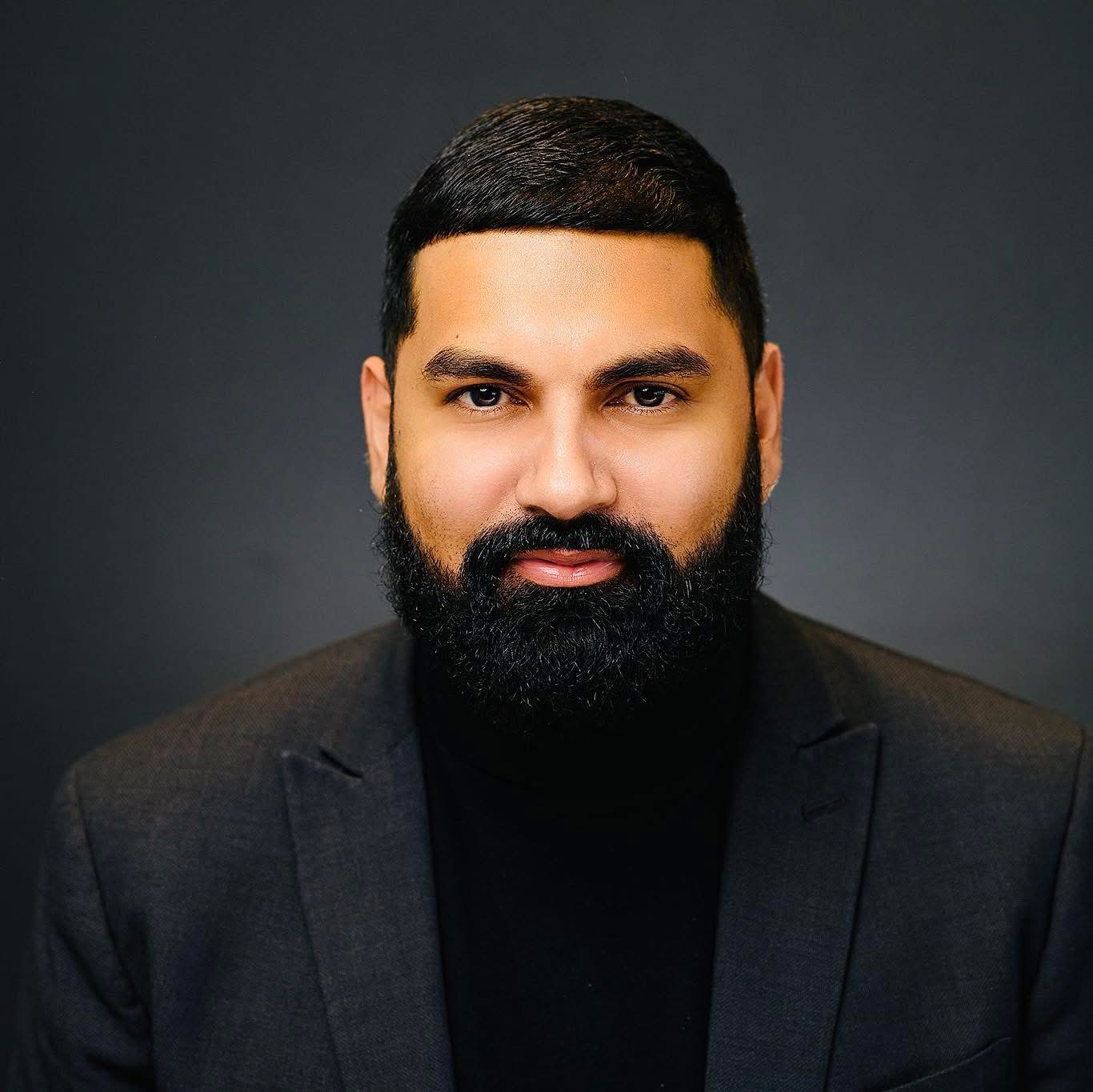 Athar Haseebullah. He is a Pakistani man with a full beard. He is wearing a black turtle neck and grey blazer.