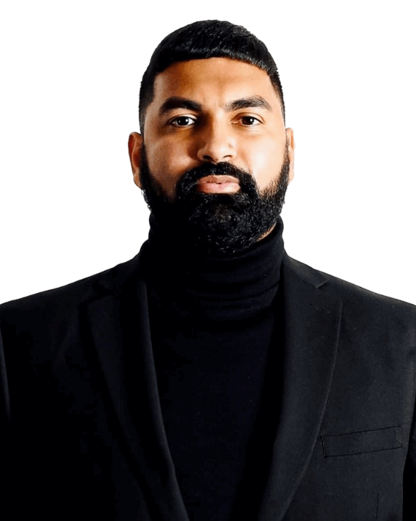A man with a neatly trimmed beard and short hair, wearing a black turtleneck and a black blazer, stands against a plain white background.