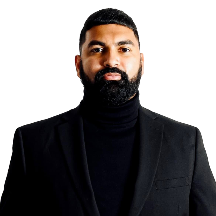 A man with a neatly trimmed beard and short hair, wearing a black turtleneck and a black blazer, stands against a plain white background.