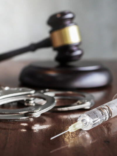 A gavel, a pair of handcuffs, and a syringe sitting on a desk.