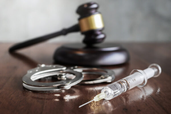 A gavel, a pair of handcuffs, and a syringe sitting on a desk.