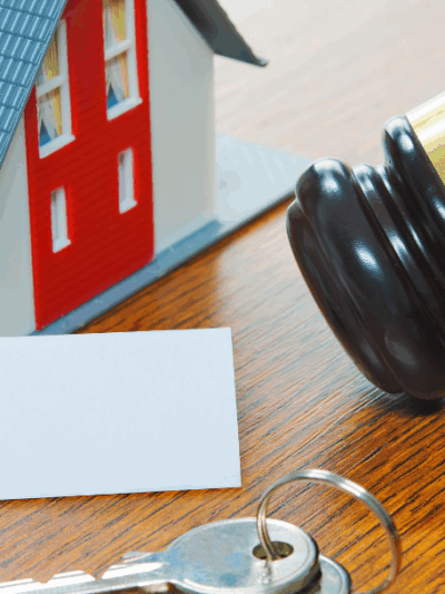 left to right: a small toy house, a deed, two keys, and a gavel sitting on a wooden surface