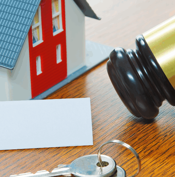 left to right: a small toy house, a deed, two keys, and a gavel sitting on a wooden surface