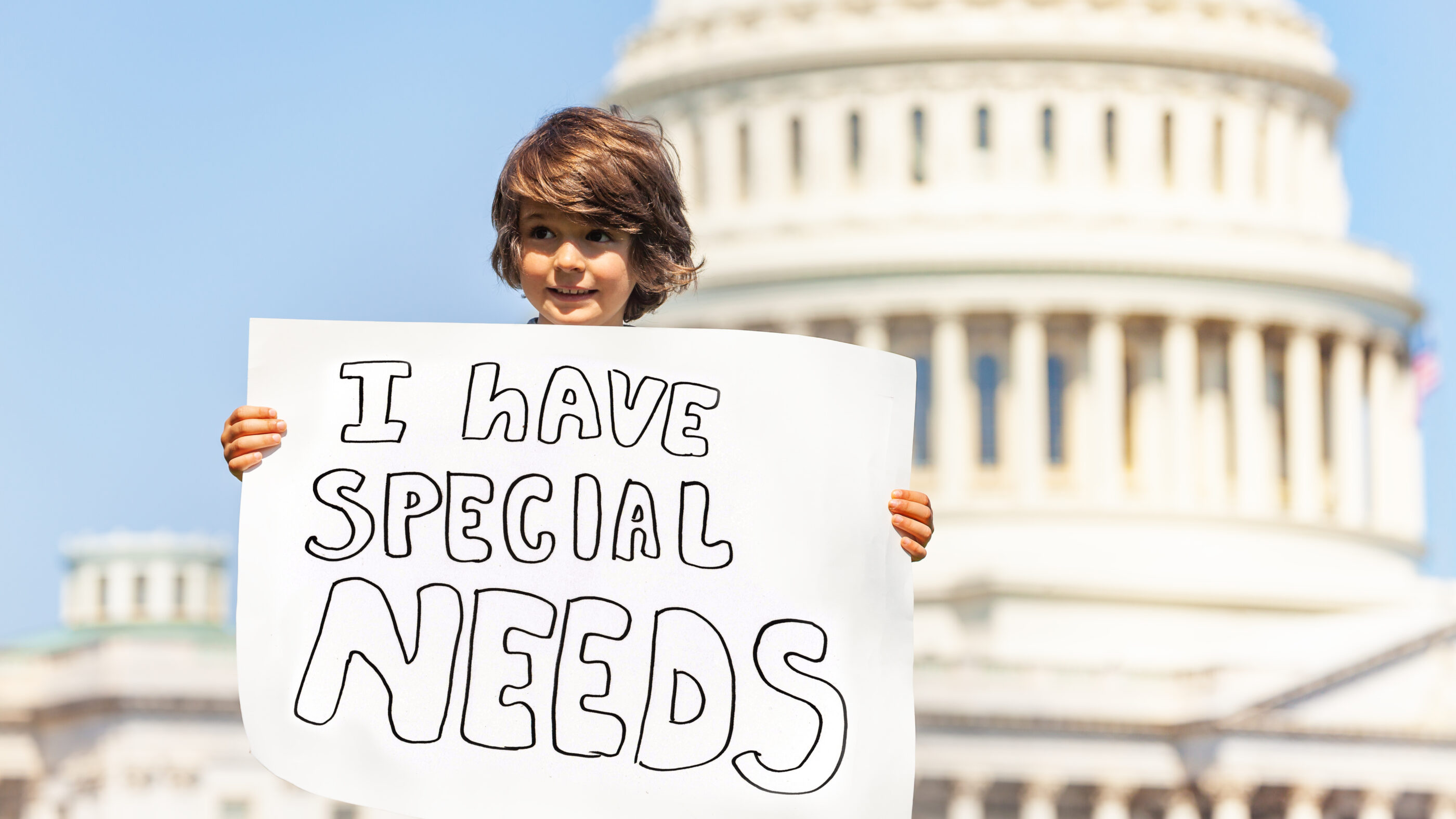 A little boy in front of the Capitol building. He is holding a sign that says "I have special needs."