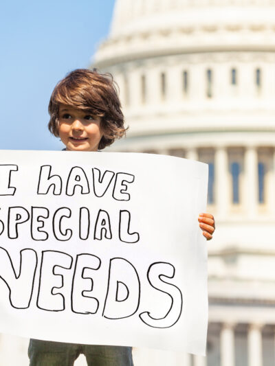 A little boy in front of the Capitol building. He is holding a sign that says "I have special needs."