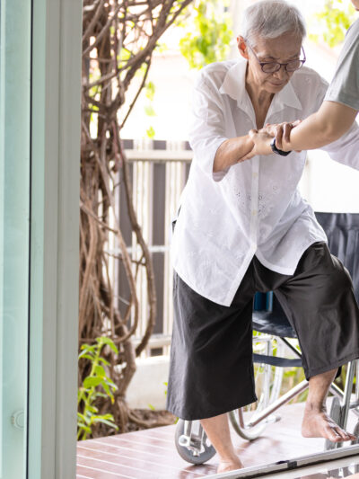 a woman helping an elderly women into the house. The doorway is a glass sliding door.