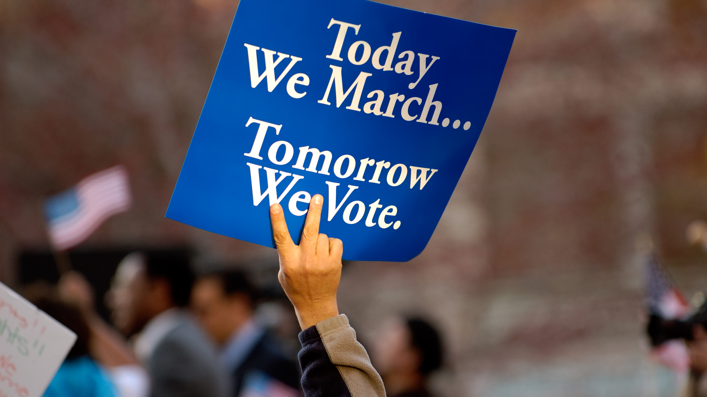 A blue sign with white text on it. It says "Today we march, tomorrow we vote."