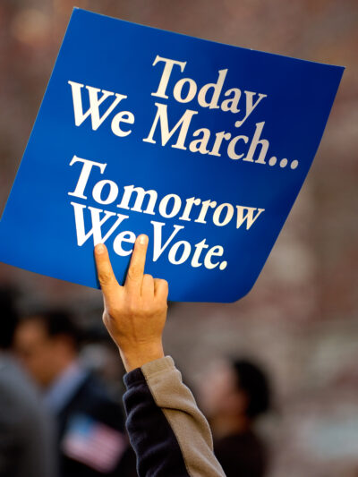 A blue sign with white text on it. It says "Today we march, tomorrow we vote."