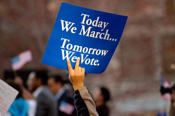 A blue sign with white text on it. It says "Today we march, tomorrow we vote."