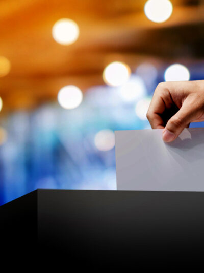 a photo a hand putting a blank paper into a ballot box. the background is blurred.
