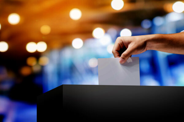 a photo a hand putting a blank paper into a ballot box. the background is blurred.