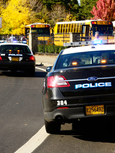 Line of police cars parked in front of school. There is also a line of school buses.