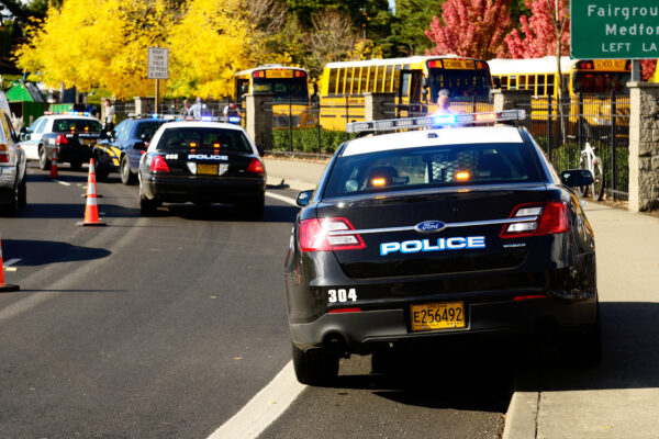 Line of police cars parked in front of school. There is also a line of school buses.