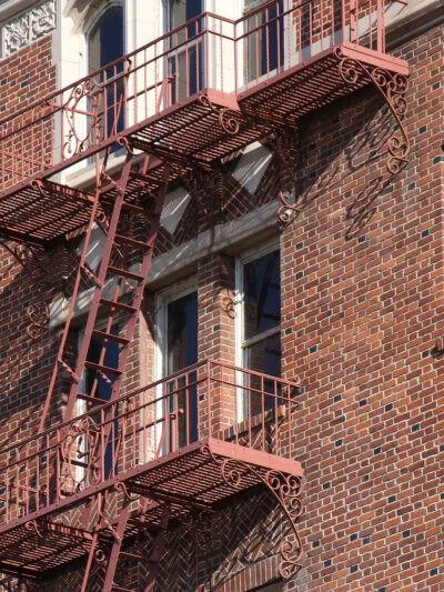 Side of apartment building made out of brick wall with fire escape going down the side.