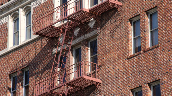 Side of apartment building made out of brick wall with fire escape going down the side.