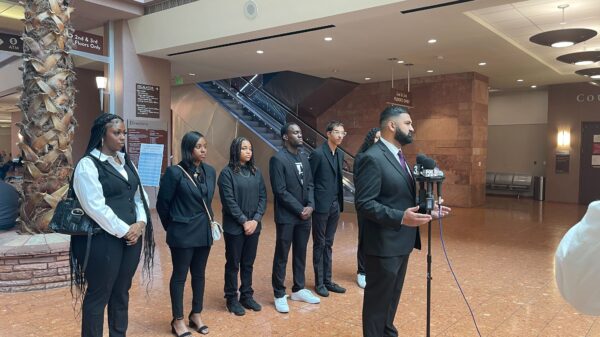 Athar Haseebullah standing at a microphone speaking to the press while the 6 Emerging Leaders Board Members stand behind him in a line.