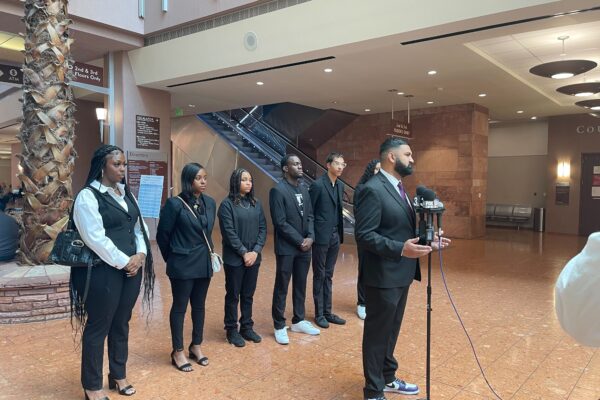 Athar Haseebullah standing at a microphone speaking to the press while the 6 Emerging Leaders Board Members stand behind him in a line.