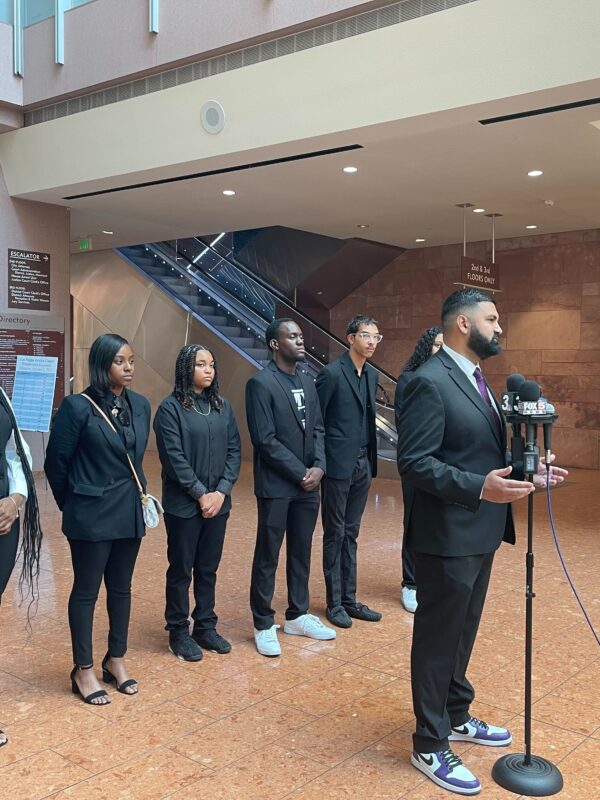 Athar Haseebullah standing at a microphone speaking to the press while the 6 Emerging Leaders Board Members stand behind him in a line.