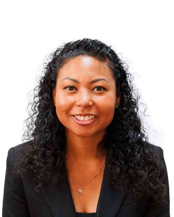 A woman with medium length black curly hair wearing a Black blazer and gold necklace smiling against a white background.