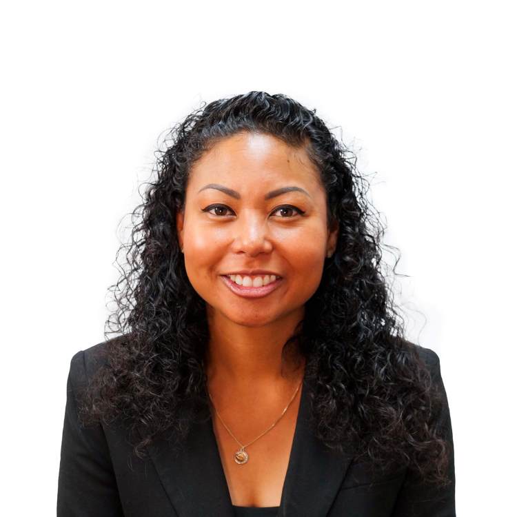 A woman with medium length black curly hair wearing a Black blazer and gold necklace smiling against a white background.