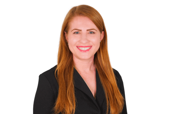 Tia in front of a white background. She is wearing a black button up. She is a white woman with red hair and blue eyes.