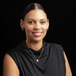 Headshot of Alex. She is a Black woman with her hair pulled back in a bun. She is wearing a black sleeveless top and a gold necklace.