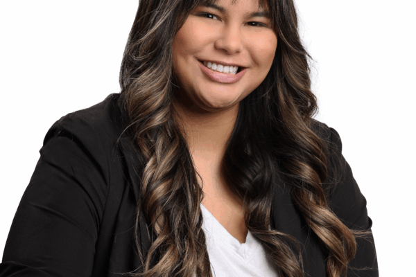 Headshot of Jordyn. She is wearing a white shirt and a black blazer. She is a brown woman with long brown hair and bangs.